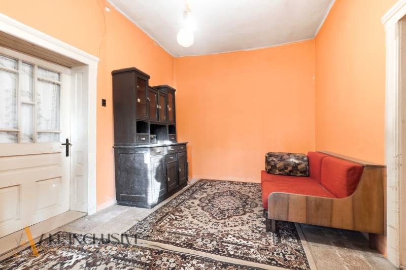 Na predaj 4-izbový rodinný dom, Dolné Saliby - Izba v rodinnom dome s oranžovými stenami, koberec, gauč a tmavá skriňa.