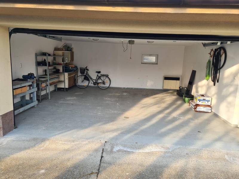 Na predaj 5-izb. rodinný dom na 50-á pozemku, Sap - Garáž v rodinnom dome v Sape s bicyklom, nástrojmi a úložnými regálmi.