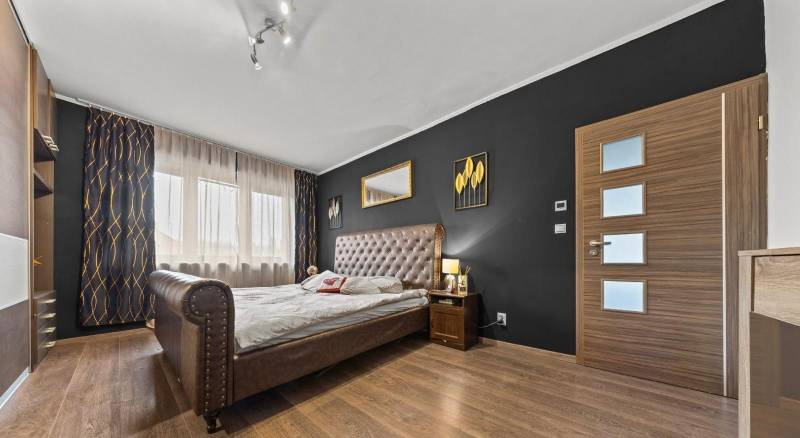 Na predaj 5-izb. rodinný dom na 50-á pozemku, Sap - Spálňa v rodinnom dome s tmavou stenou, veľkou posteľou a podlahou s dreveným dekorom.