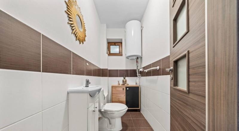 Na predaj 5-izb. rodinný dom na 50-á pozemku, Sap - Toaleta v rodinnom dome s dekoratívnym zrkadlom, drevenými dvierkami a hnedými obkladmi.