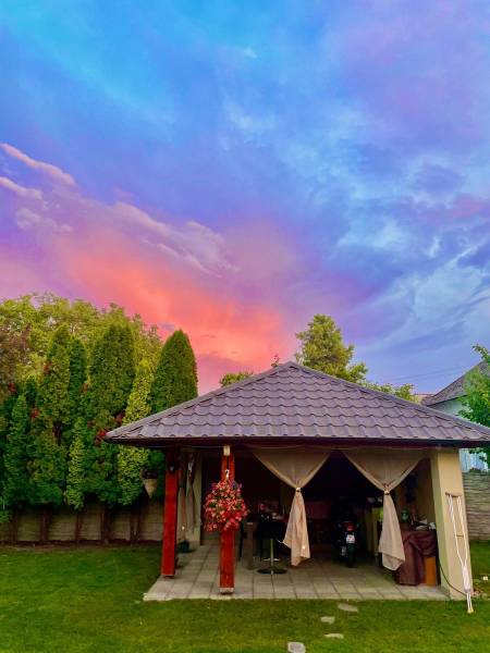 Na predaj 5-izb. rodinný dom na 50-á pozemku, Sap - Záhradný altánok pri rodinnom dome v Sape pod farebnou oblohou s tujami v pozadí.