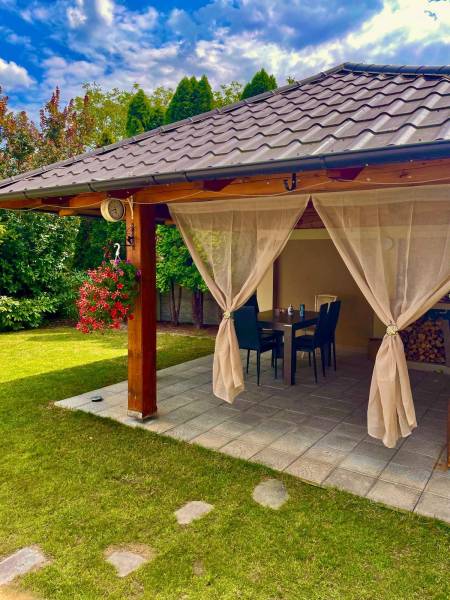 Na predaj 5-izb. rodinný dom na 50-á pozemku, Sap - Záhradná terasa rodinného domu v Sape so stolom, stoličkami a závesmi.