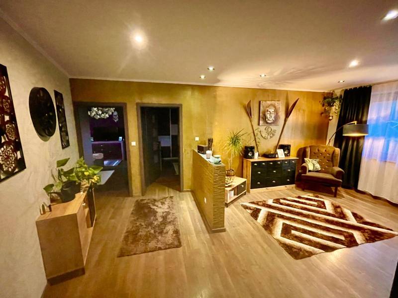 Na predaj 5-izb. rodinný dom na 50-á pozemku, Sap - Interiér rodinného domu s podlahou s dreveným dekorom, kreslo, dekorácie a rastliny.