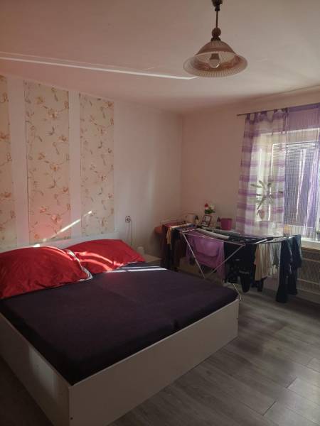 Na predaj 3-izb. rodinný dom, Gabčíkovo – Polná ulica - Spálňa v rodinnom dome s posteľou, dekoratívnou tapetou a podlahou s dreveným dekorom.