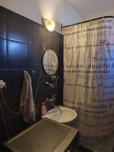 Na predaj 3-izb. rodinný dom, Gabčíkovo – Polná ulica - Kúpeľňa v rodinnom dome s tmavými obkladačkami, umývadlom a sprchovacím závesom.