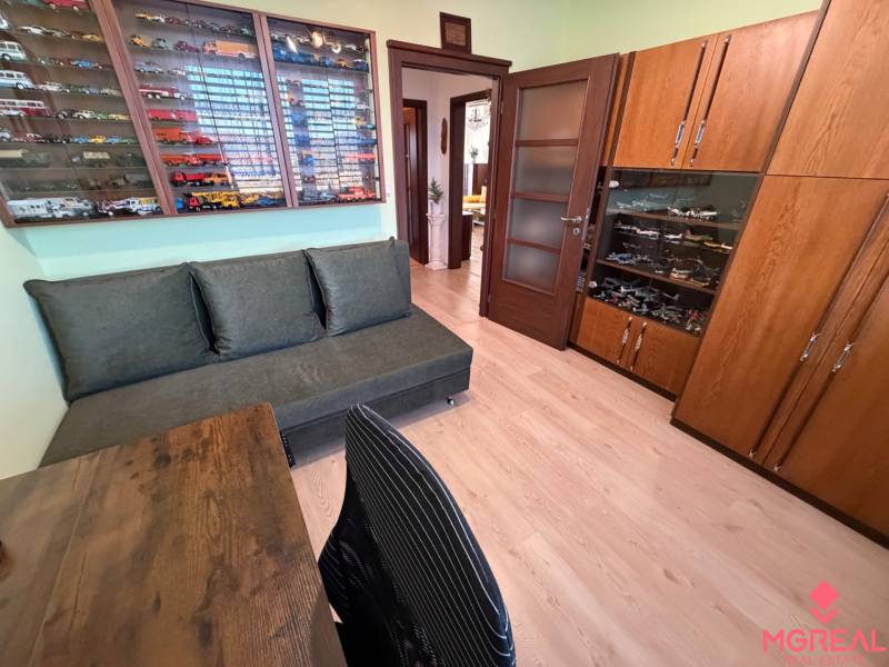 3 izbový byt s balkónom Topoľčany  - Izba s pohovkou, vitrínou s modelmi a podlahou s dreveným dekorom v 3-izbovom byte.