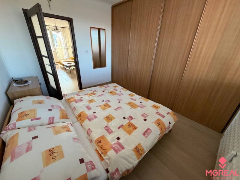 3 izbový byt s balkónom Topoľčany  - Spálňa v 3-izbovom byte s posteľou, vstavanou skriňou a podlahou s dreveným dekorom.