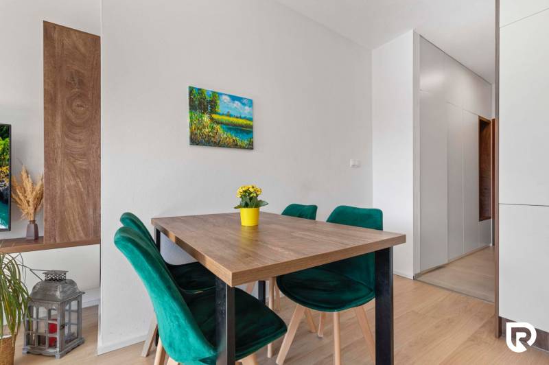 | Krásny a moderný 2-izbový byt | 51,50m² | - Jedálenský kút s dreveným stolom, zelenými stoličkami a podlahou s dreveným dekorom v 2-izbovom byte.
