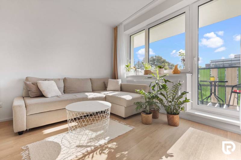 | Krásny a moderný 2-izbový byt | 51,50m² | - Obývačka v 2-izbovom byte s pohovkou, rastlinami a balkónom, podlaha s dreveným dekorom.