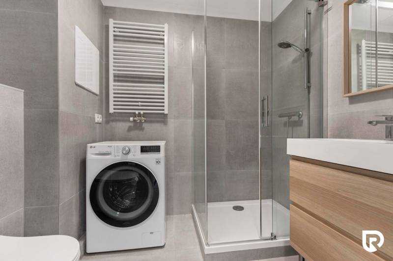 | Krásny a moderný 2-izbový byt | 51,50m² | - Kúpeľňa v 2-izbovom byte so sprchovým kútom, práčkou a umývadlom na drevenej skrinke.