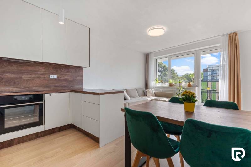 | Krásny a moderný 2-izbový byt | 51,50m² | - Svetlá kuchyňa s obývačkou, drevený dekor, jedálenský stôl a zelené stoličky v 2-izbovom byte.