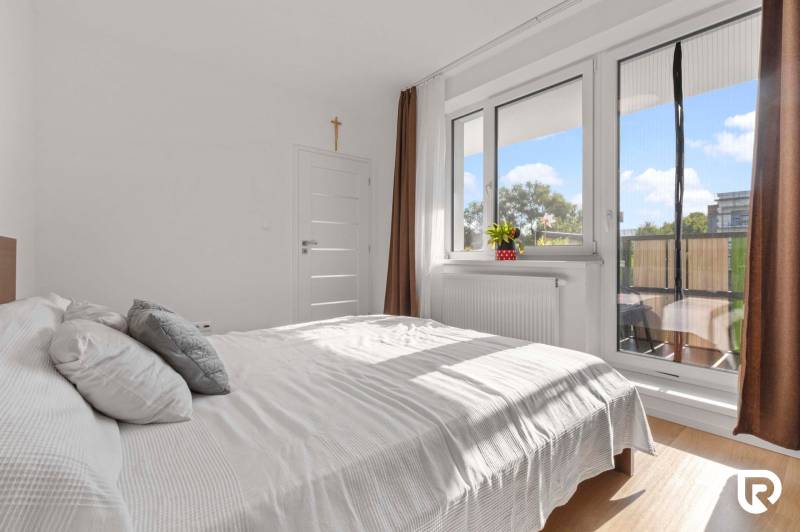 | Krásny a moderný 2-izbový byt | 51,50m² | - Svetlá spálňa v 2-izbovom byte s posteľou, balkónom a podlahou s dreveným dekorom.