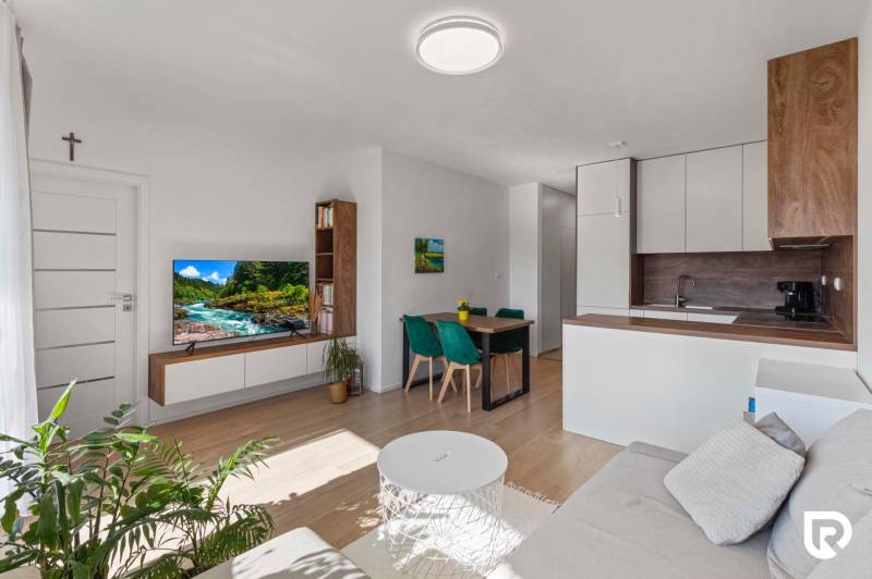 | Krásny a moderný 2-izbový byt | 51,50m² | - Obývacia izba 2-izbového bytu s podlahou s dreveným dekorom, televízorom a jedálenským stolom.