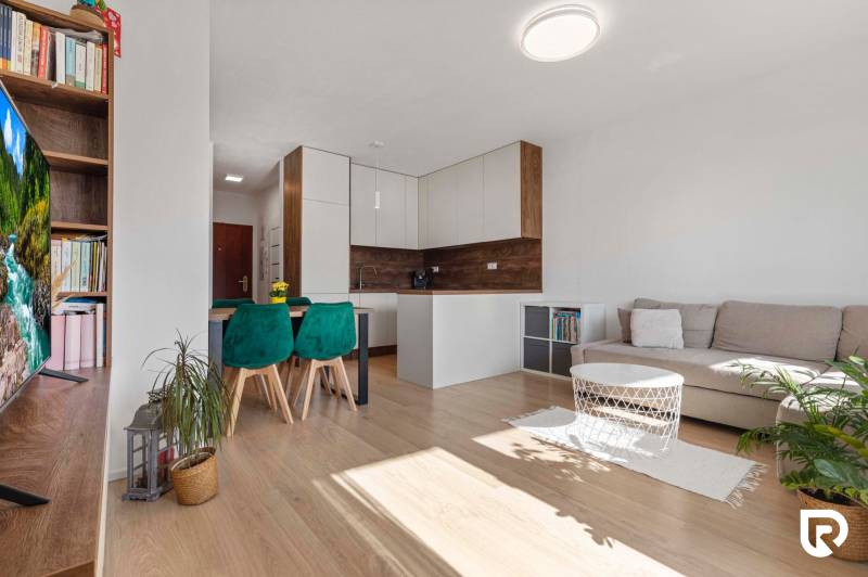 | Krásny a moderný 2-izbový byt | 51,50m² | - Obývacia izba s kuchyňou v 2-izbovom byte, podlaha s dreveným dekorom, zelenými stoličkami.