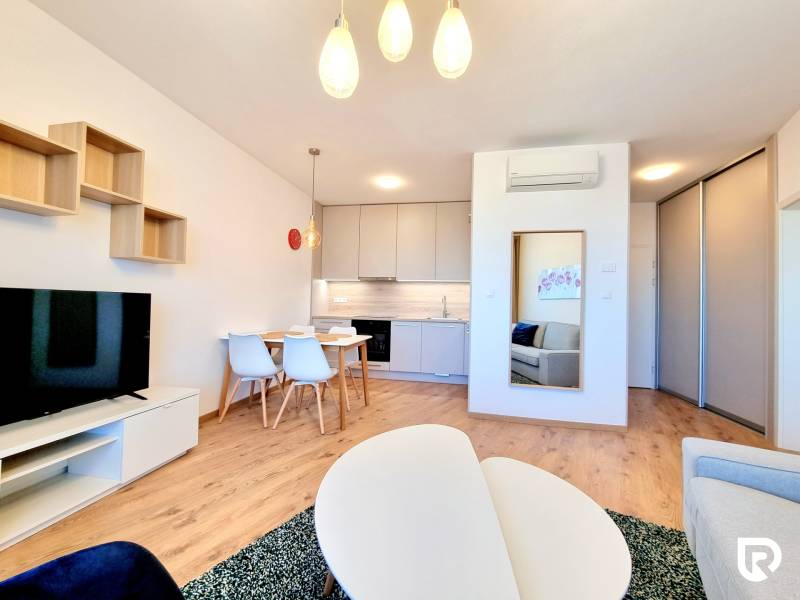 Posledný investičný krásny 2-izbový byt | 55 m² | RÍNOK RAČA - Obývacia izba v 2-izbovom byte s podlahou s dreveným dekorom, kuchyňou a jedálenským stolom.