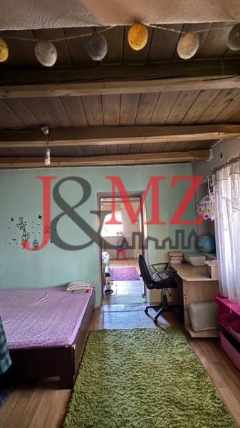 Útulný rodinný dom v tichej lokalite Mýtnych Ludán (MK-4) - Izba s podlahou s dreveným dekorom, posteľou, pracovným stolom a dekoračnými trámami na strope.