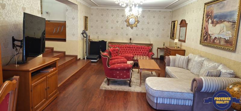 Luxusný rodinný dom s bazénom a dvojgarážou v Komárne - Obývacia izba v rodinnom dome s červeným nábytkom a televízorom na podlahe s dreveným dekorom.