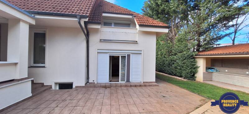 Luxusný rodinný dom s bazénom a dvojgarážou v Komárne - Rodinný dom v Komárne s terasou, záhradou a bielymi okenicami.