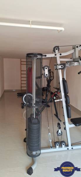 Luxusný rodinný dom s bazénom a dvojgarážou v Komárne - Fitness miestnosť s posilňovacími strojmi v rodinnom dome má svetlý keramický povrch.