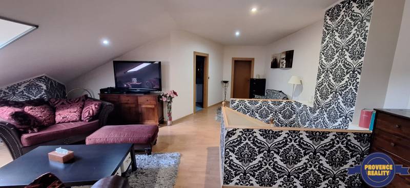 Luxusný rodinný dom s bazénom a dvojgarážou v Komárne - Obývacia izba v rodinnom dome s pohovkou, vzorovanou tapetou a TV.