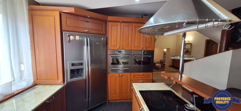 Luxusný rodinný dom s bazénom a dvojgarážou v Komárne - Kuchyňa v rodinnom dome s drevenými skrinkami a nerezovými spotrebičmi.