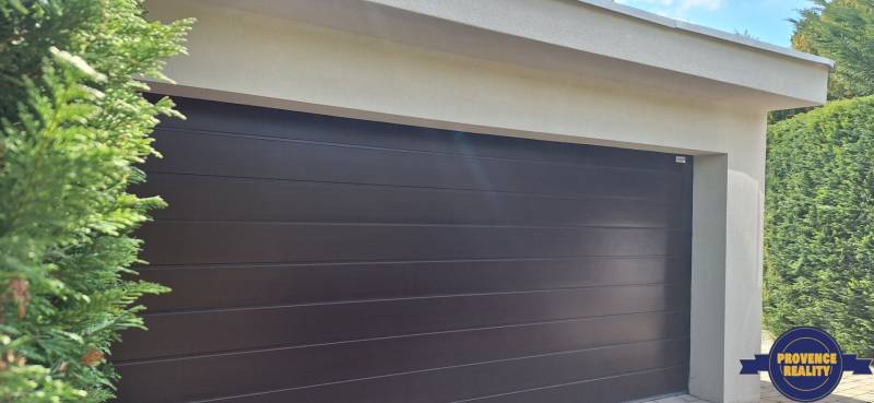 Luxusný rodinný dom s bazénom a dvojgarážou v Komárne - Garážové dvere pri rodinnom dome v Komárne, obklopené zeleňou.