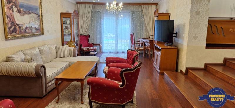 Luxusný rodinný dom s bazénom a dvojgarážou v Komárne - Obývacia izba v rodinnom dome s červenými kreslami a podlahou s dreveným dekorom.