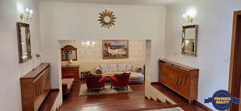 Luxusný rodinný dom s bazénom a dvojgarážou v Komárne - Luxusný interiér rodinného domu s dreveným dekorom, pohovkou a umeleckými dielami na stenách.