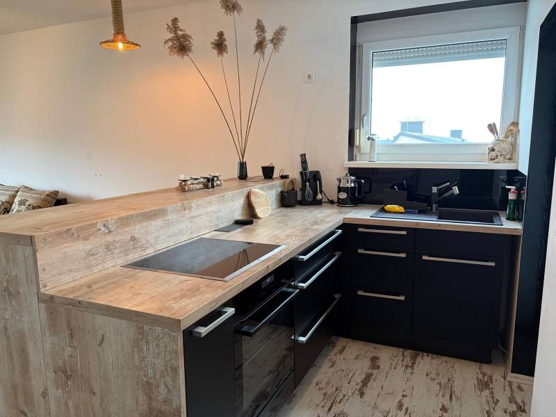 Zariadený 3 izbový byt s balkónom v Kittsee  - Kuchyňa v 3-izbovom byte s čiernymi skrinkami a podlahou s dreveným dekorom.