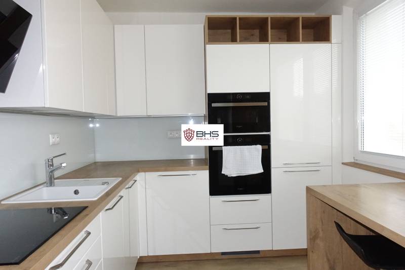 PRENÁJOM –  1 izba (príp. 2 izby) v 3-izb. byte, Gwerkovej ul., BA V - Moderná kuchyňa s bielymi skrinkami a podlahou s dreveným dekorom v 3-izbovom byte.