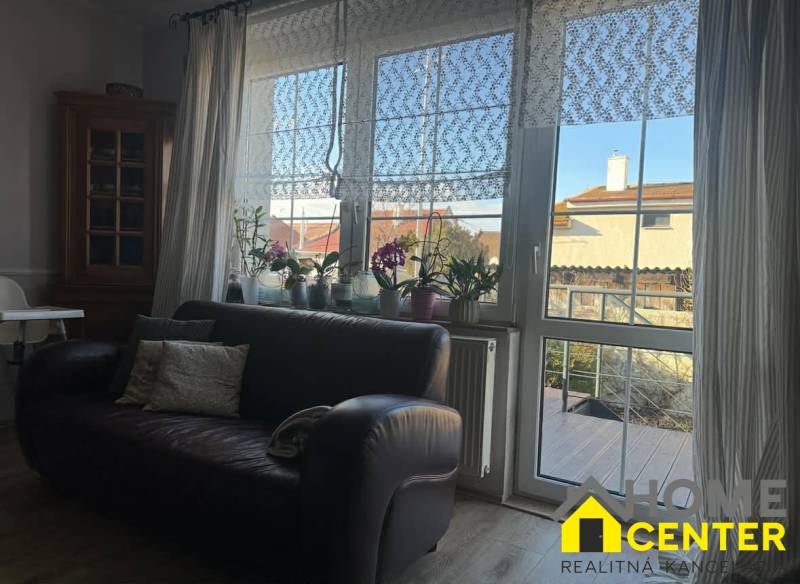 PREDAJ : RODINNÝ DOM, KOMÁRNO - Kožená sedačka a okno s čipkovanými závesmi v Rodinnom dome s podlahou s dreveným dekorom.