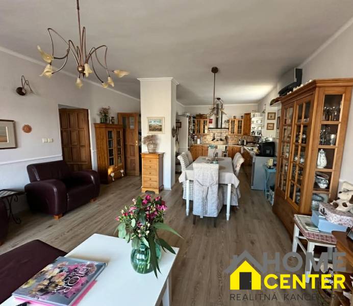 PREDAJ : RODINNÝ DOM, KOMÁRNO - Obývacia izba s kuchyňou v rodinnom dome, podlaha s dreveným dekorom, kvetiny na stole.