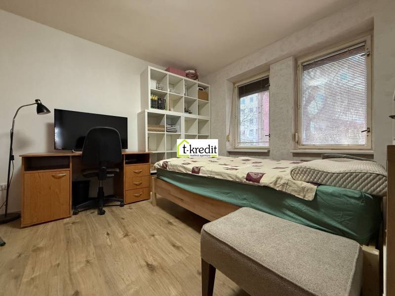 PREDAJ - 2i BYT - ZLATÉ MORAVCE - Izba v 2-izbovom byte s posteľou, pracovným stolom a podlahou s dreveným dekorom.