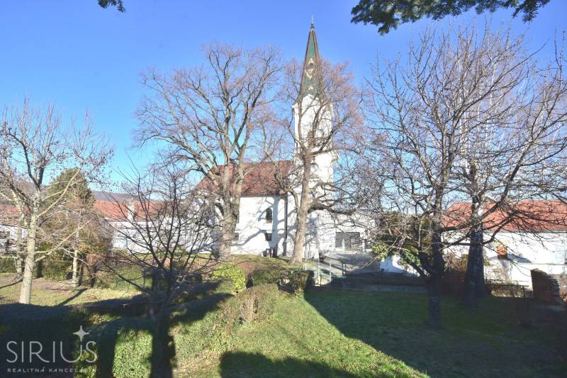 LIMBACH, 176 m2 –  kompletne zrekonštruovaný 5-i rodinný dom - Starý kostol s vežou, stromy bez listov, okolie s trávnatým porastom.