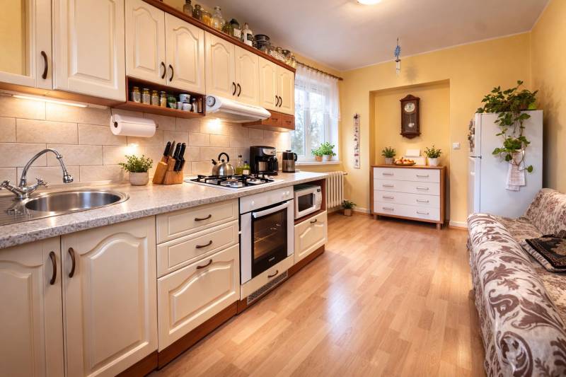 REZERVONY - 2 izbový tehlový byt na Novej Dubnici, 60  - Kuchyňa v 2-izbovom byte s podlahou s dreveným dekorom, svetlá linka a rastliny.