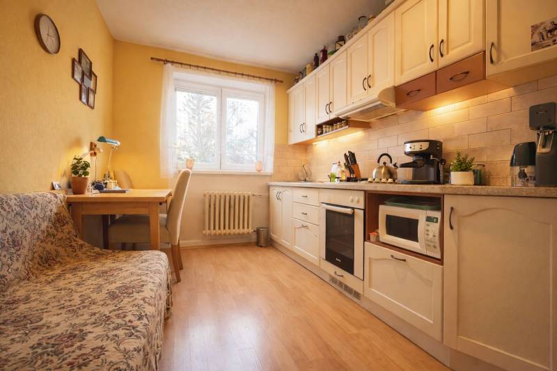 REZERVONY - 2 izbový tehlový byt na Novej Dubnici, 60  - Kuchyňa v 2-izbovom byte s dreveným dekorom podlahy, svetlým nábytkom a jedálenským kútom.