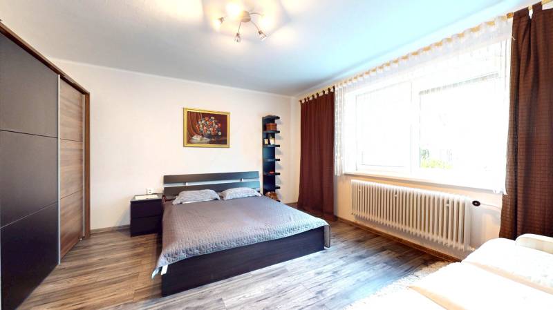 Prerobený rodinný dom na veľkom tichom pozemku v obci Pruské   - Spálňa v rodinnom dome s posteľou, skrinkou, obrazom a podlahou s dreveným dekorom.