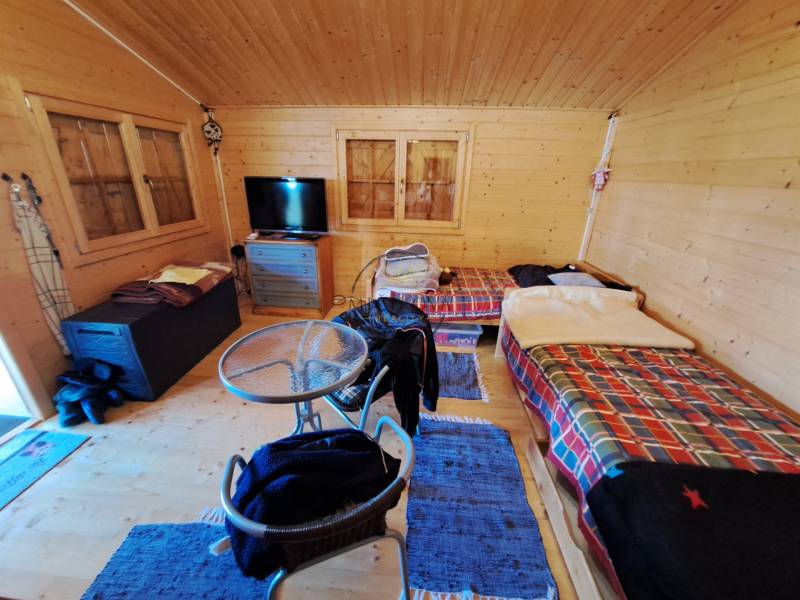 Predáme záhradu so zrubovou chatou, Nitra - Dolné Krškany - Izba v Záhradách so stolíkom, stoličkami a dvomi posteľami s farebnými prikrývkami.