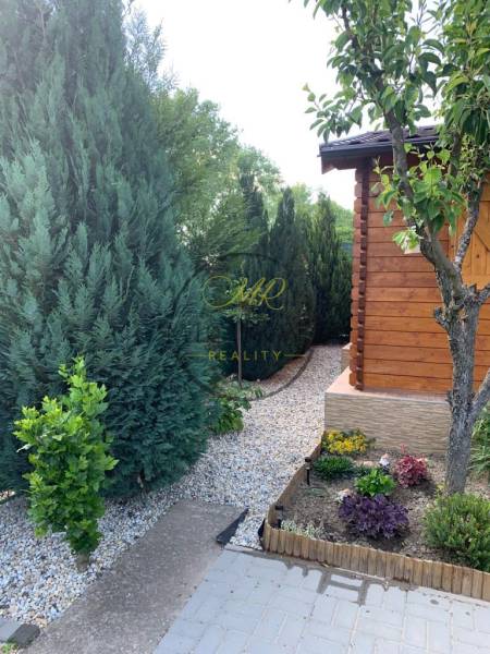 Predáme záhradu so zrubovou chatou, Nitra - Dolné Krškany - Záhrady v Dolných Krškanoch, Nitra s upravenými ihličnanmi a dreveným záhradným domčekom.