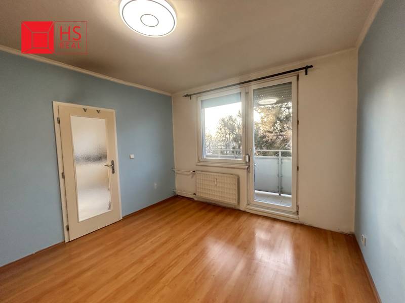 Predaj 3 izb. bytu s balkónom v NZ - Izba v 3-izbovom byte s podlahou s dreveným dekorom a balkónom.