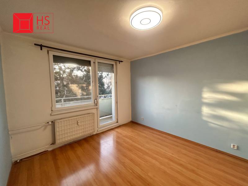 Predaj 3 izb. bytu s balkónom v NZ - Izba s podlahou s dreveným dekorom a balkónom v 3-izbovom byte.