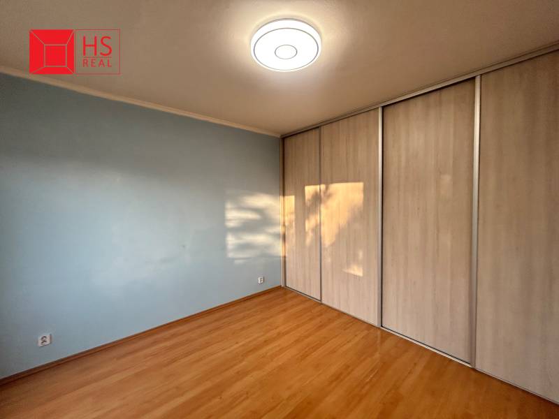 Predaj 3 izb. bytu s balkónom v NZ - Izba s podlahou s dreveným dekorom a vstavanou skriňou v 3-izbovom byte.