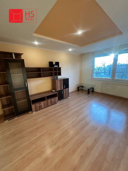 Predaj 3 izb. bytu s balkónom v NZ - Obývacia izba s podlahou s dreveným dekorom a nábytkom v 3-izbovom byte.