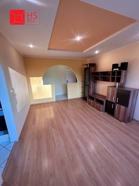 Predaj 3 izb. bytu s balkónom v NZ - Obývacia izba v 3-izbovom byte s podlahou s dreveným dekorom a vstavaným osvetlením.