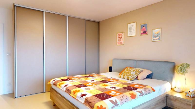 Novozariadený rodinný dom s veľkými spálňami i šatníkom pri Trenčíne   - Spálňa v rodinnom dome s posteľou, vstavanou skriňou a dekoratívnymi obrazmi na stene.