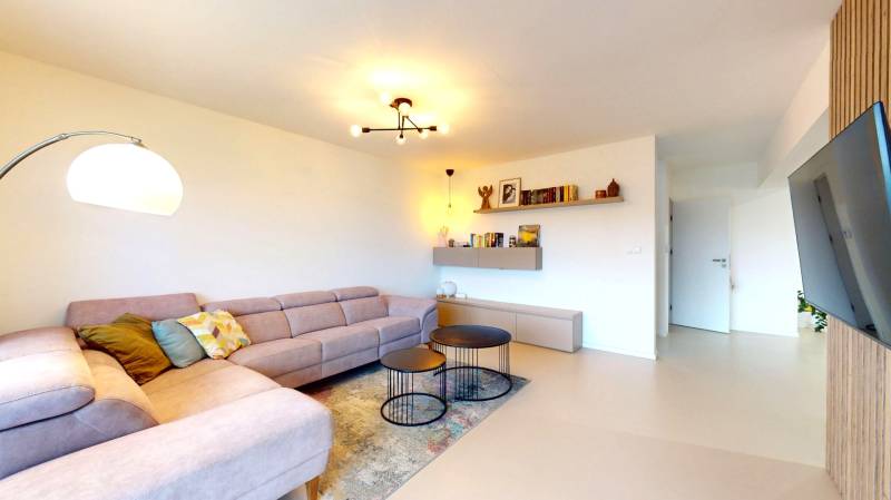 Novozariadený rodinný dom s veľkými spálňami i šatníkom pri Trenčíne   - Obývačka v rodinnom dome s rohovou sedačkou, okrúhlymi stolíkmi a podlahou s dreveným dekorom.