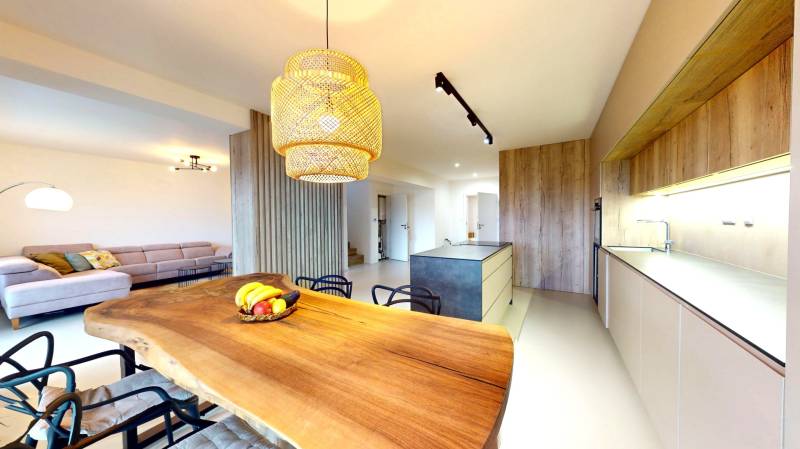 Novozariadený rodinný dom s veľkými spálňami i šatníkom pri Trenčíne   - Kuchyňa v rodinnom dome s dreveným stolom, pohovkou a moderným osvetlením.