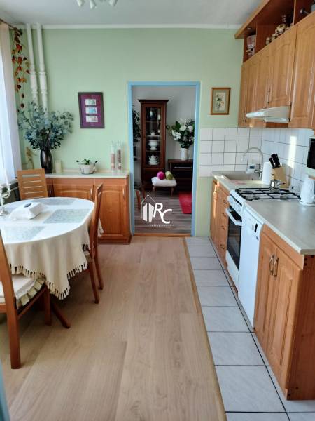 2 izbový byt na Severe - Kuchyňa v 2-izbovom byte s podlahou s dreveným dekorom a stolom v rohu miestnosti.