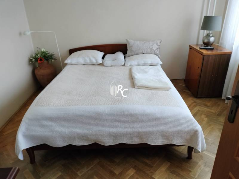 2 izbový byt na Severe - Spálňa s manželskou posteľou, podlahou s dreveným dekorom a nočným stolíkom v 2-izbovom byte.