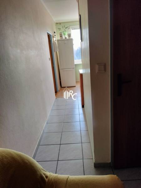 2 izbový byt na Severe - Chodba s chladničkou v 2-izbovom byte, dlažba na podlahe, svetlé steny.